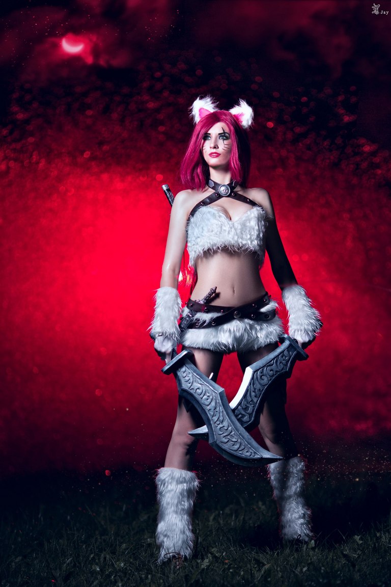 A person dressed in a furry, fantasy-themed costume with pink hair and a pair of large, decorative swords against a dramatic red background.