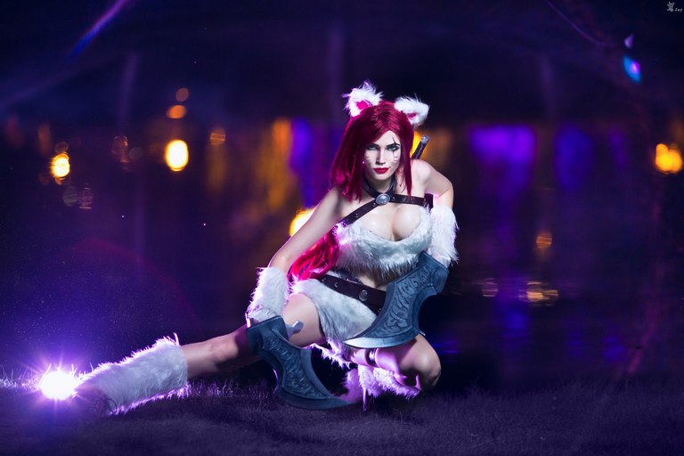 Cosplayer dressed as a character with red hair and animal-themed attire, posing with large weapons in a dramatic setting with purple lighting.