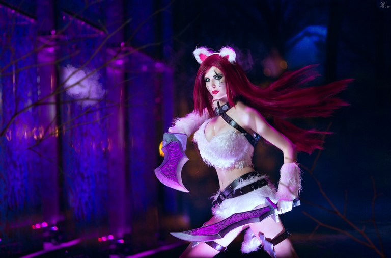 A person in a fantasy costume with furry accessories holding dual curved blades in a dimly lit environment, surrounded by purple and blue lighting.