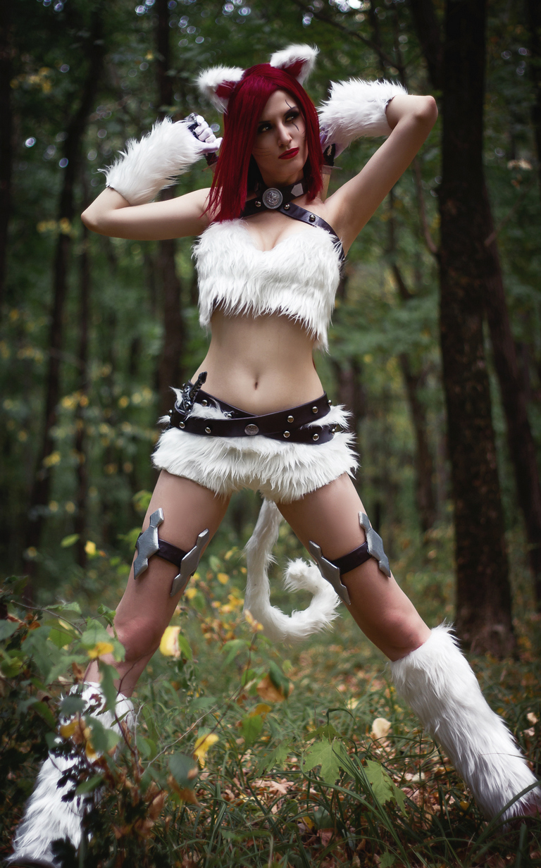 A person dressed in a furry costume with cat-like features, posing in a forested setting.