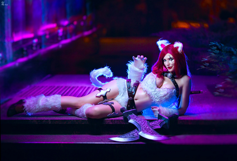 A person in a furry cat costume with red hair poses dramatically, holding two large, ornate blades, against a colorful, illuminated background.