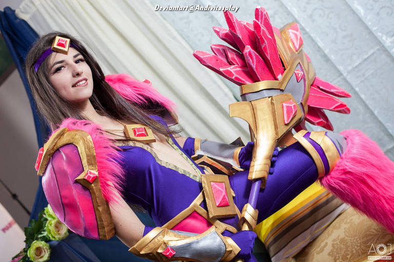 A person dressed in a colorful fantasy costume featuring a purple outfit with pink fur accents and elaborate armor, posing confidently.