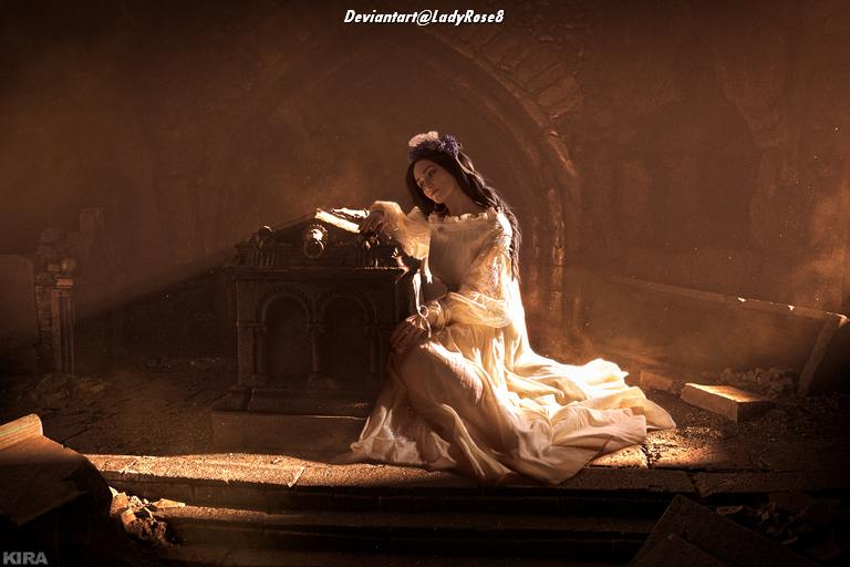 A woman in a flowing white dress sits near an ornate tomb in a dimly lit, atmospheric space with beams of light filtering through dust.