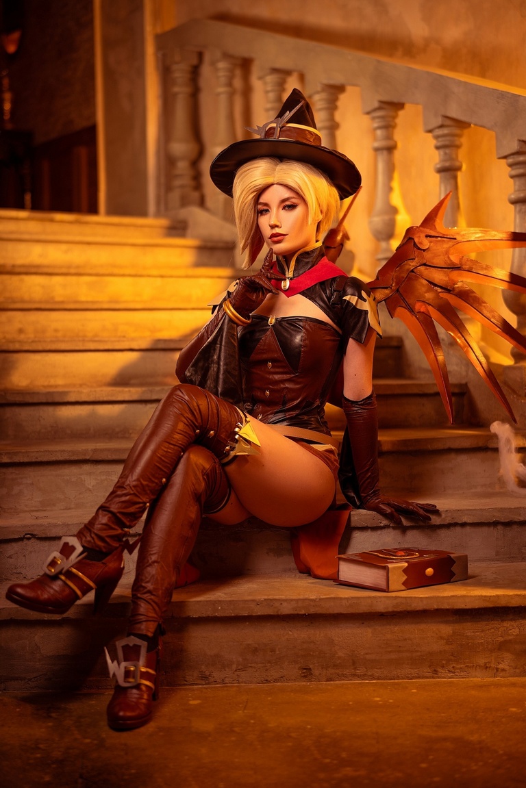A woman in a fantasy costume with a witch's hat and angelic wings sits confidently on a staircase, styled with atmospheric lighting.