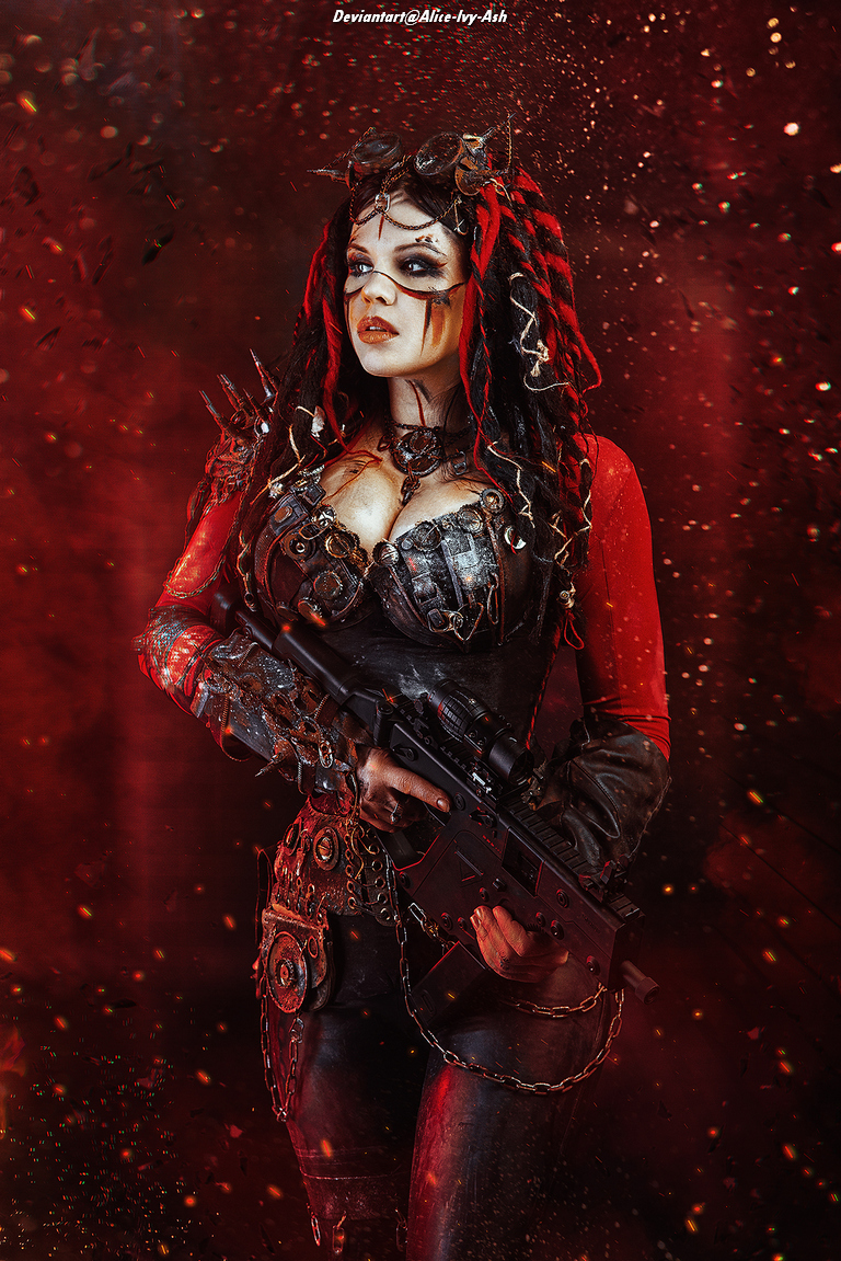 A woman in an elaborate post-apocalyptic costume with red and black accents, holding a modern rifle, set against a dramatic red background with sparks and debris.