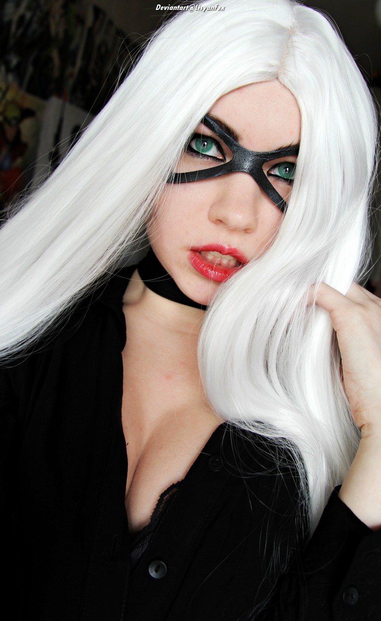 Close-up portrait of a person with long white hair and striking green eyes, wearing a black mask and a dark shirt, posing confidently.