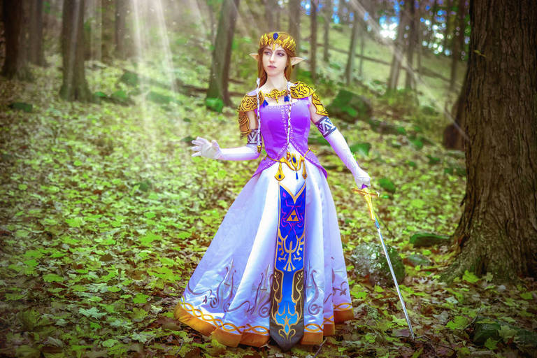A person dressed as Princess Zelda from a video game, standing in a lush forest with sunlight filtering through the trees.