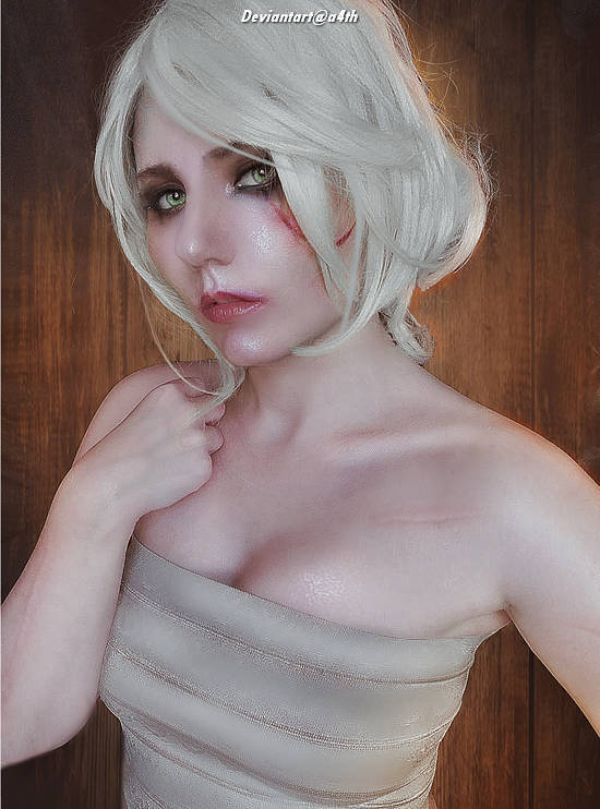 A close-up portrait of a person with short white hair, wearing a strapless beige top, with a soft expression, against a wooden background.