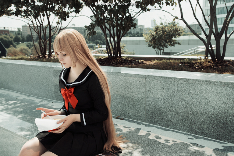 A girl with long hair, wearing a school uniform with a bow, sits on a bench, looking down at a bowl in her hands, surrounded by greenery.