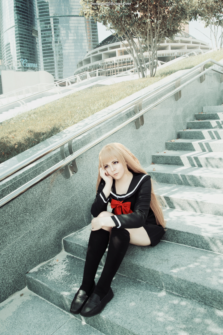 A young person in a school uniform with a red bow sitting on stairs, looking contemplative. Modern buildings are visible in the background.