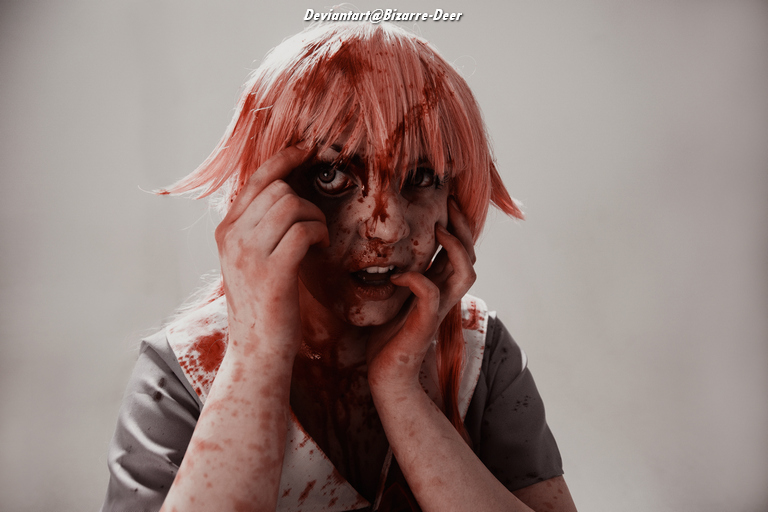 A person with pink hair and a distressed expression, covered in fake blood, holding their face with both hands.