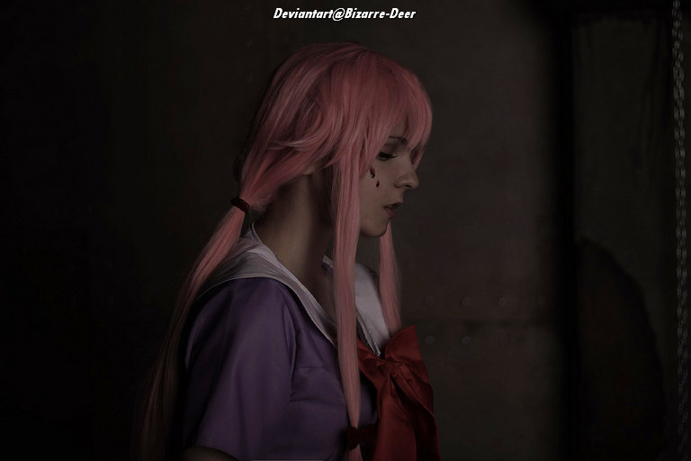 A person with long pink hair is wearing a purple outfit, looking down with a pensive expression. They have a small tear painted on their cheek, and the background appears dark and industrial.