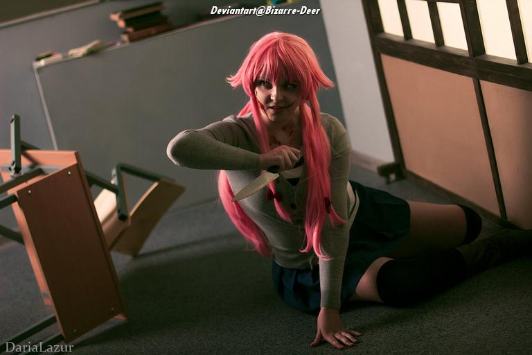 A person with pink hair, dressed in a school uniform, sits on the floor with a knife in hand, surrounded by overturned furniture.
