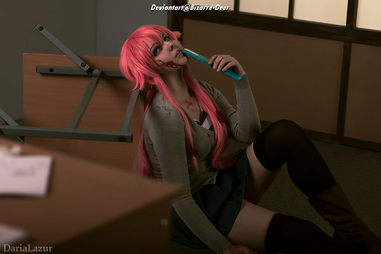 A person with long pink hair wearing a gray top and a dark skirt sits on the floor next to an overturned desk. They hold a blue toothbrush to their mouth, with a smeared face resembling a scary character. The background features a minimalistic interior with soft lighting.