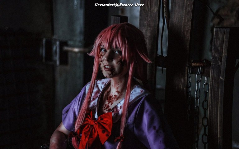 A young person with pink hair, wearing a purple outfit and a red bow, sitting in a dimly lit room with a distressed expression. Their face and outfit are smeared with fake blood, adding to a dramatic and eerie atmosphere.