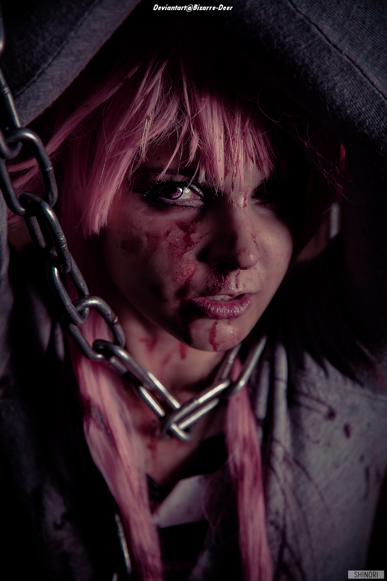 A close-up portrait of a person with pink hair, featuring dramatic lighting and facial makeup resembling blood and dirt. The individual is chained, with a serious expression, creating a dark and intense atmosphere.