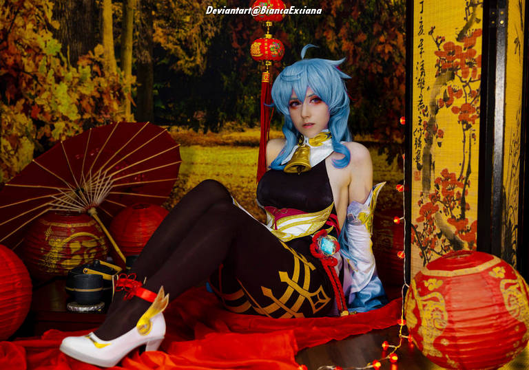 A person in a colorful costume with blue hair poses gracefully in a decorative setting featuring red lanterns and traditional props.