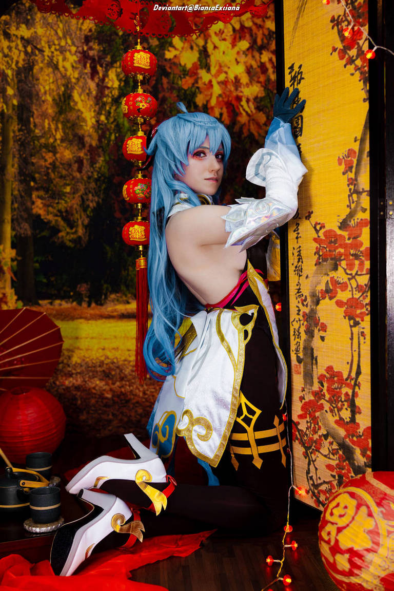 A cosplayer posing in a costume with blue hair and intricate outfit, surrounded by festive decorations like red lanterns and a backdrop featuring autumn scenery.