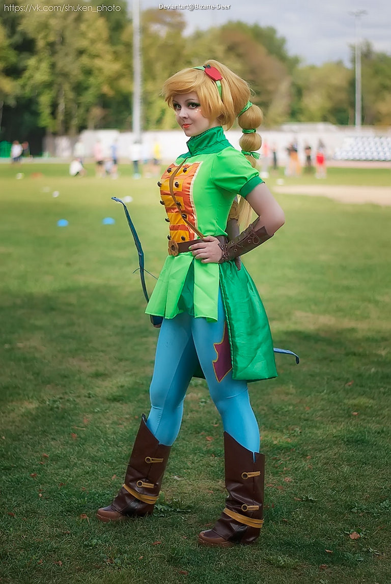 A person dressed in a vibrant green outfit with a playful design resembling a video game character, standing confidently on a grassy field.