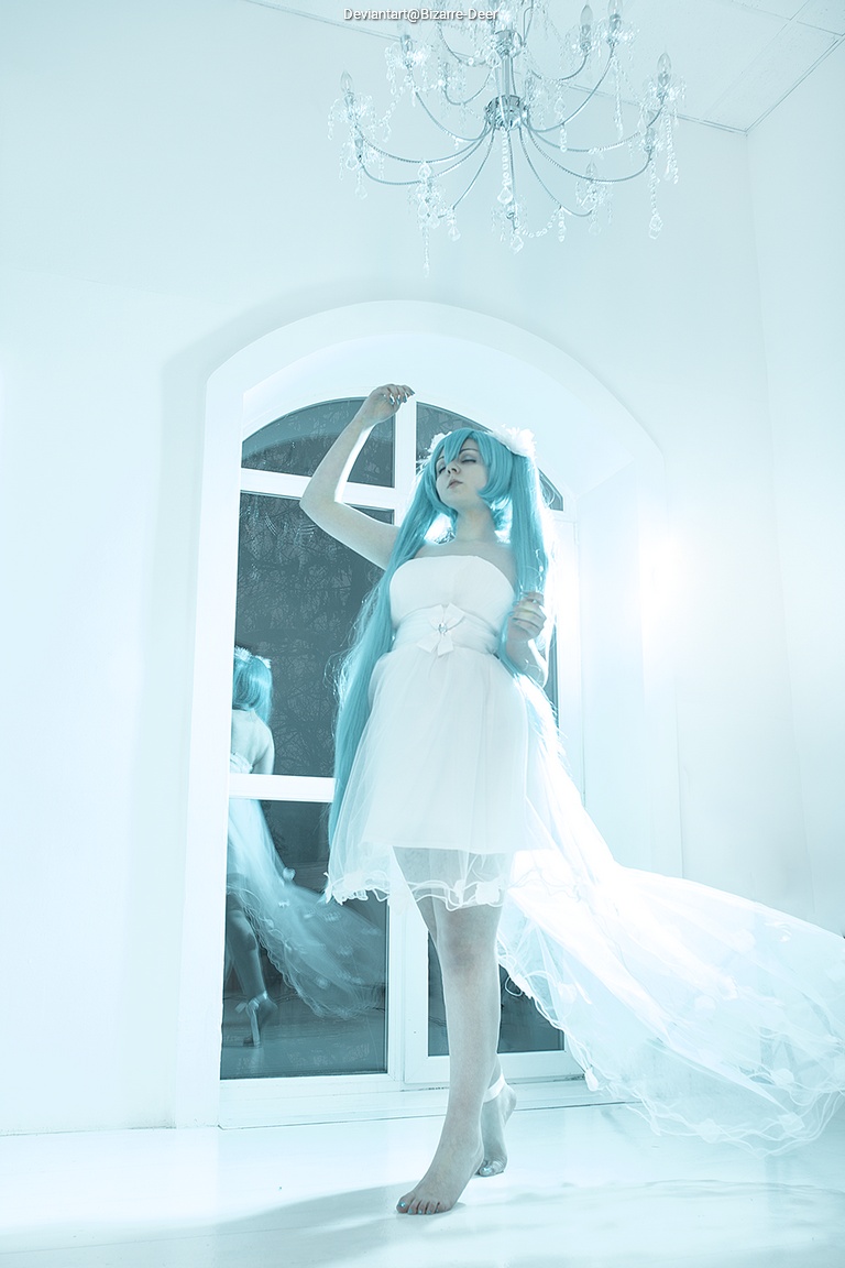 A person with long aqua-colored hair wearing a white dress stands gracefully in a bright, airy room. The dress features a flowing train, and the background includes a large window and a chandelier, adding to the ethereal atmosphere.