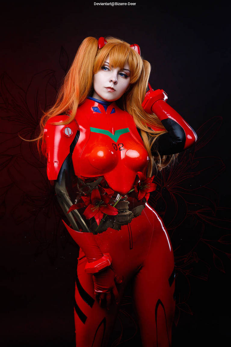 Cosplay of a character in a red suit with floral accents, featuring long blonde hair and striking makeup, set against a dark background.