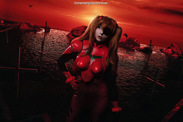 A person in a red sci-fi costume stands near a body of water during sunset, with rocky formations and crosses in the background.