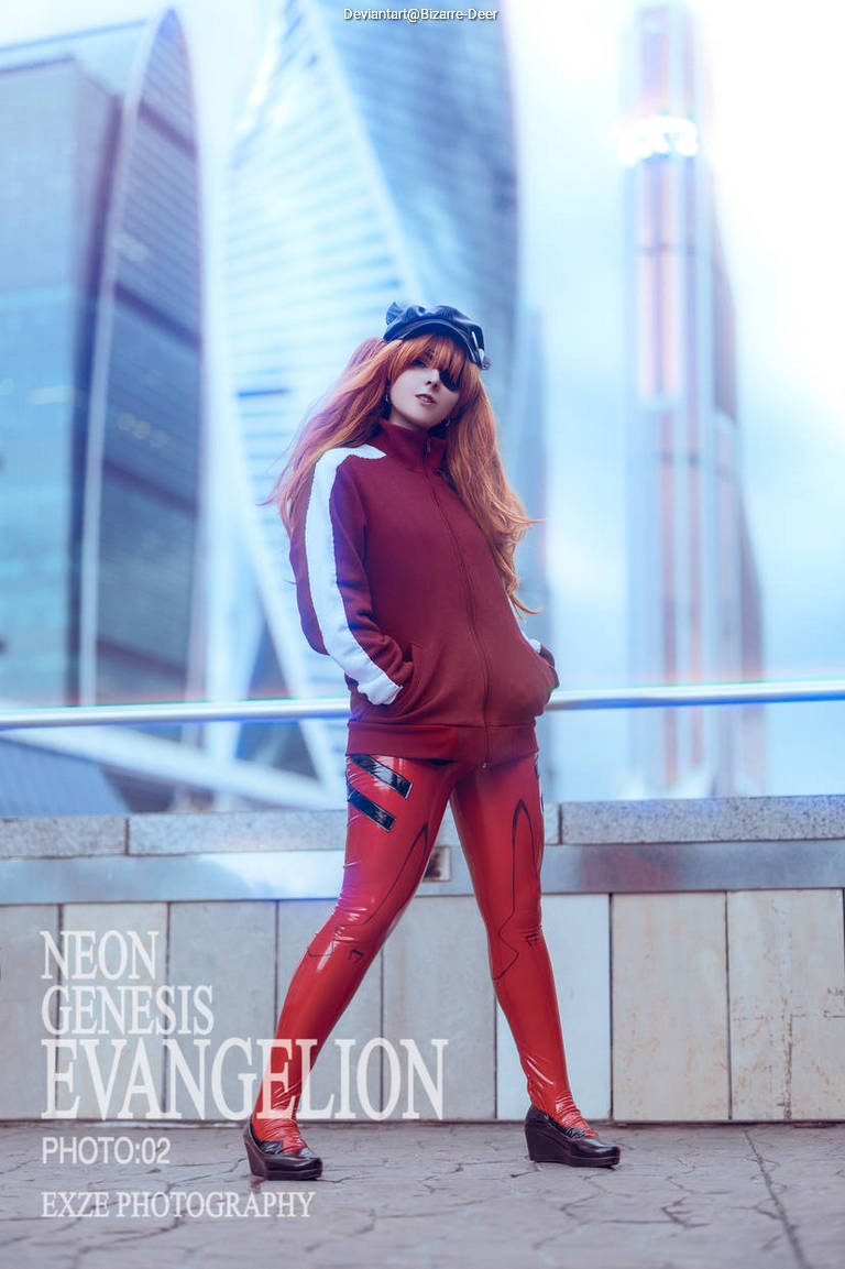 A cosplayer dressed as Asuka from Neon Genesis Evangelion, standing confidently in front of modern architecture. The costume features a red and black outfit with shiny leggings, complemented by a loose red jacket and stylish shoes.