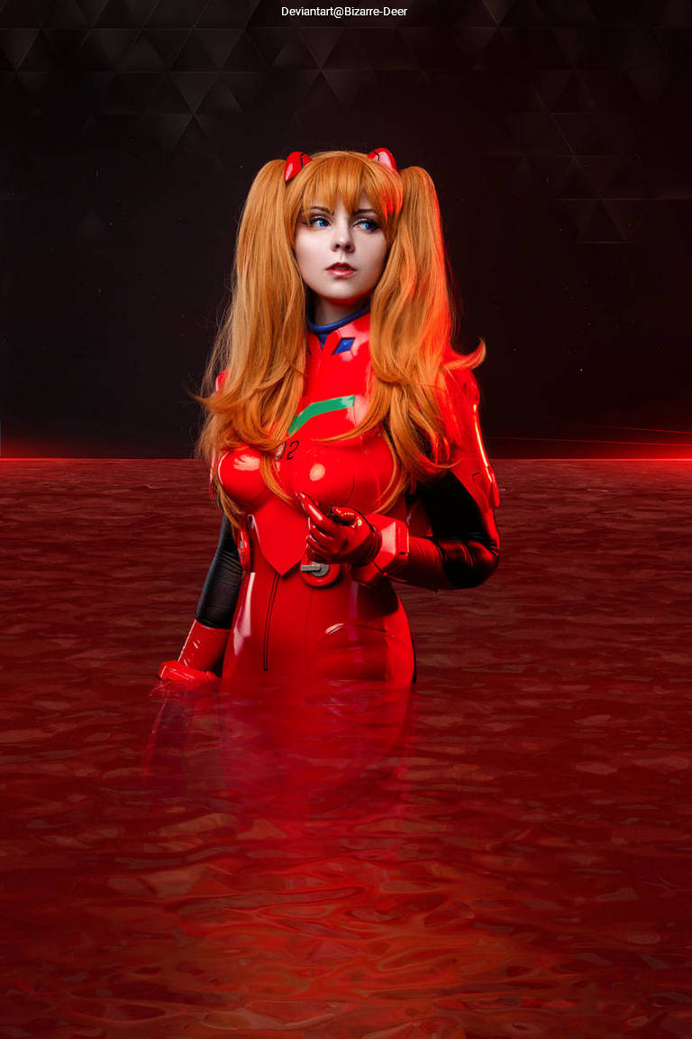 Cosplayer dressed as Asuka Langley Soryu from Neon Genesis Evangelion, standing in red water with a striking red suit and long orange hair.