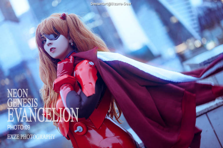 A cosplayer dressed as Asuka from Neon Genesis Evangelion, wearing a red suit and a purple cape, poses confidently in an urban setting.