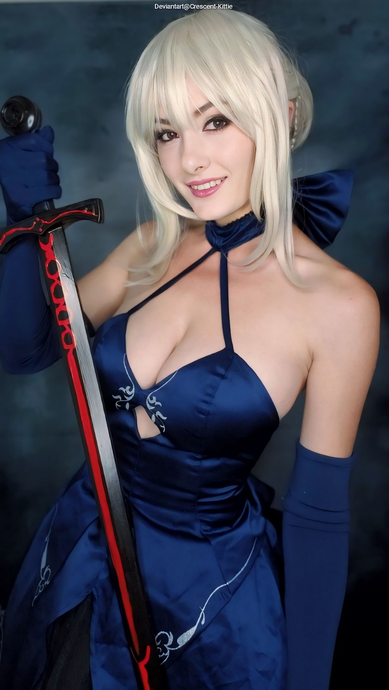 A smiling person with blonde hair wearing a blue dress and holding a sword.