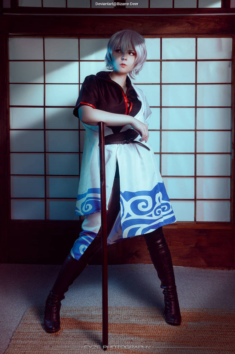 A character in a traditional setting, wearing a black and white outfit with blue accents, posing confidently with a long stick.