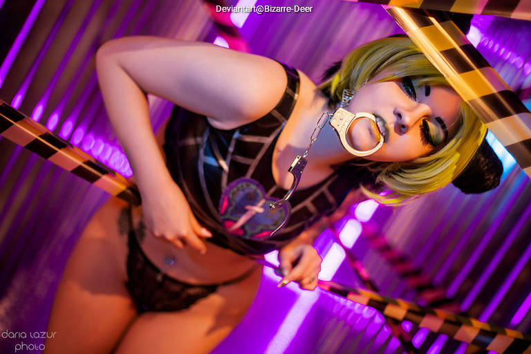 A model wearing a black outfit and neon accessories poses playfully in a colorful, vibrant setting with purple lighting.