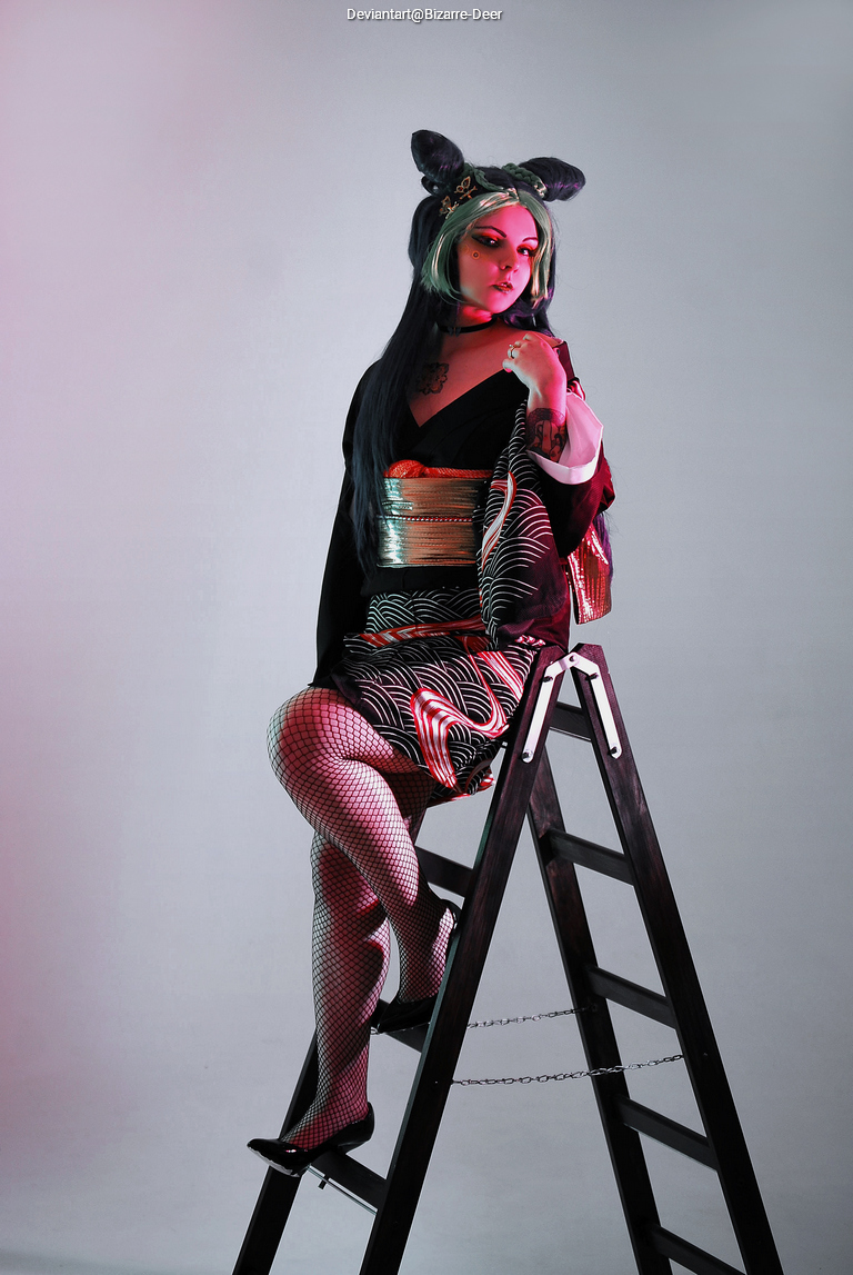 A person dressed in a stylish kimono and fishnet stockings is posing on a wooden ladder, with colorful lighting in the background.