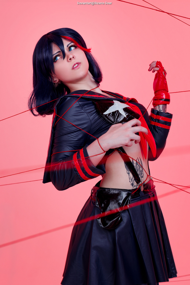A person in a black and red costume poses dynamically against a pink background, with red strings wrapped around them.