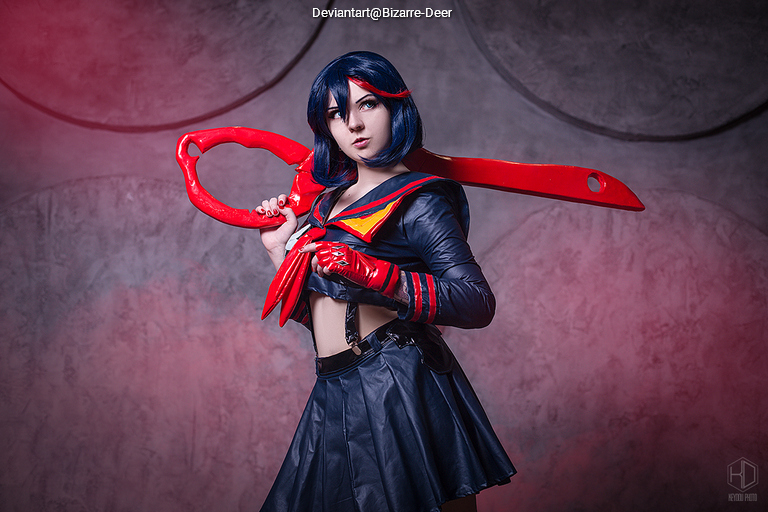 A cosplay portrait of a character featuring a black and red outfit with a large red scissor-like weapon, set against a softly lit background.