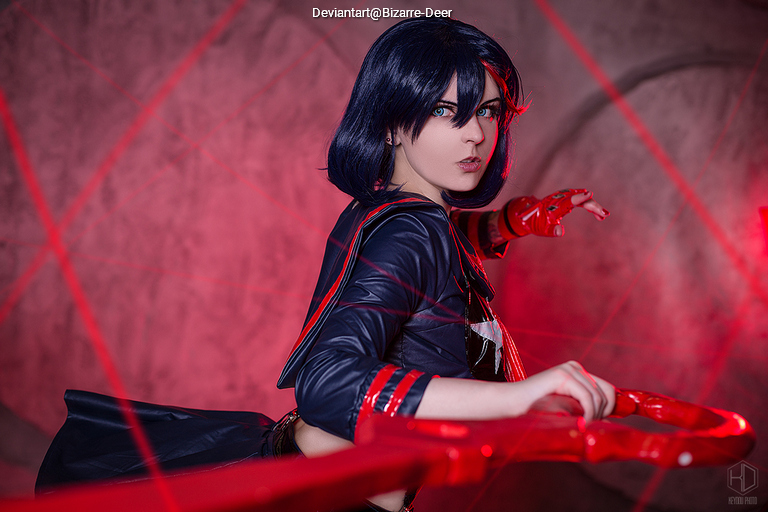 A person dressed in a dark, stylish outfit with red accents striking a pose in a dramatic setting with red light and laser beams in the background.