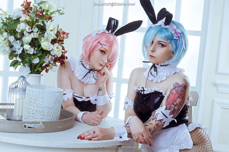 Two women in bunny costumes with pastel hair, sitting at a table with flowers and a decorative lantern.