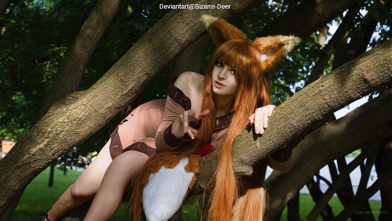 A person dressed in a playful animal costume with fox ears and a bushy tail is posing on a tree branch, surrounded by greenery.