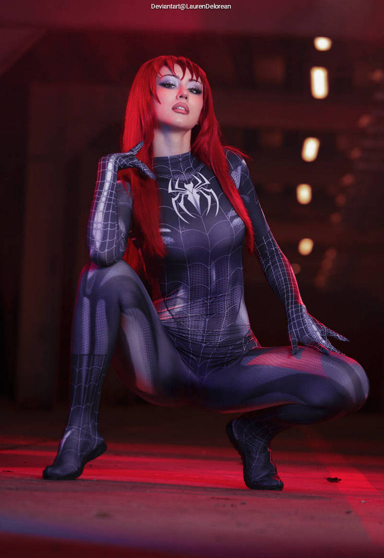 A person in a spider-themed costume with a red wig poses dramatically in a dimly lit setting, creating an artistic and vibrant atmosphere.