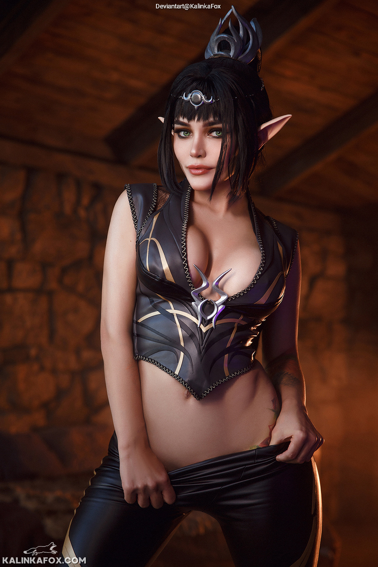 A woman in a fantasy-themed outfit with dark clothing and decorative elements, posing confidently in a dimly lit room.