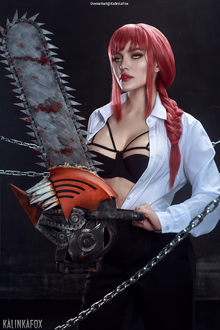 A person with red hair styled in braids is holding a chainsaw, wearing a black top and an unbuttoned white shirt. The background is dark, enhancing the dramatic effect of the image.