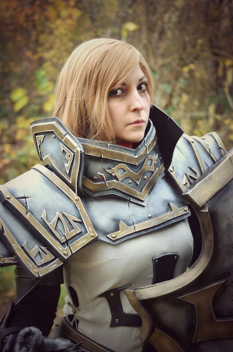 A person wearing intricate armor cosplay with a serious expression, standing in a natural outdoor setting.