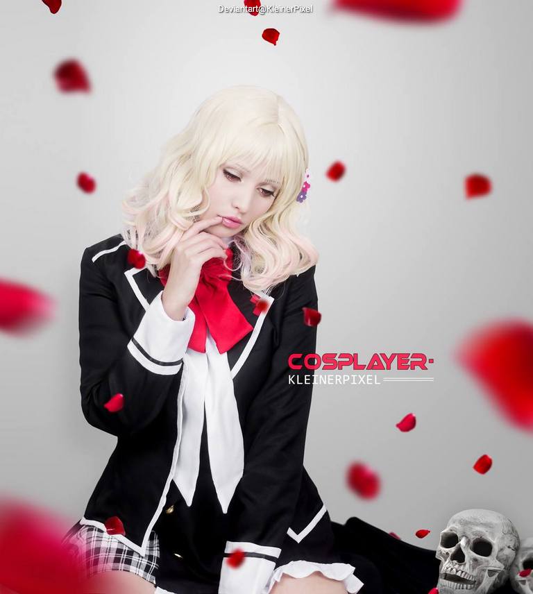 A blonde cosplayer with wavy hair sitting in a black school uniform, surrounded by falling rose petals and a skull in the foreground.
