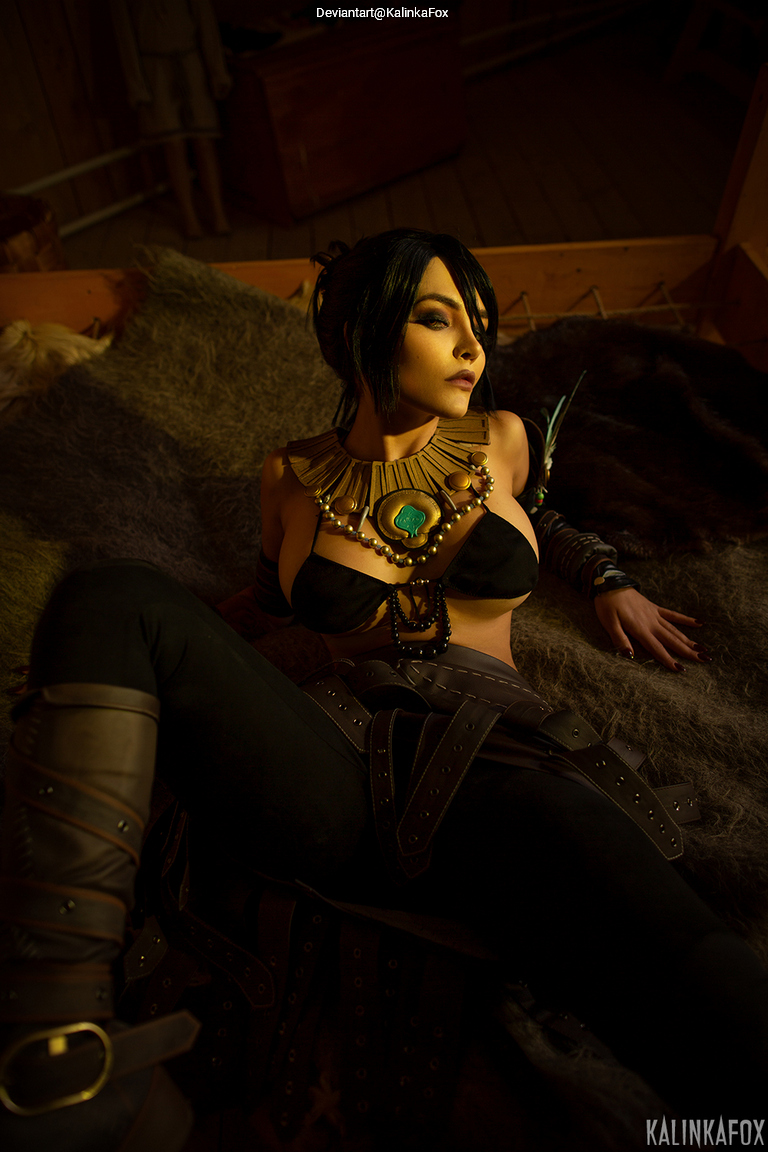 A person in a dark outfit with intricate jewelry, lying on a fur surface in a dimly lit room.