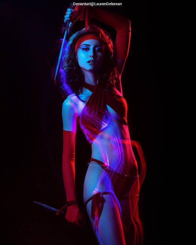 A figure in dramatic lighting, wearing a red outfit and holding a sword, posed against a dark background.