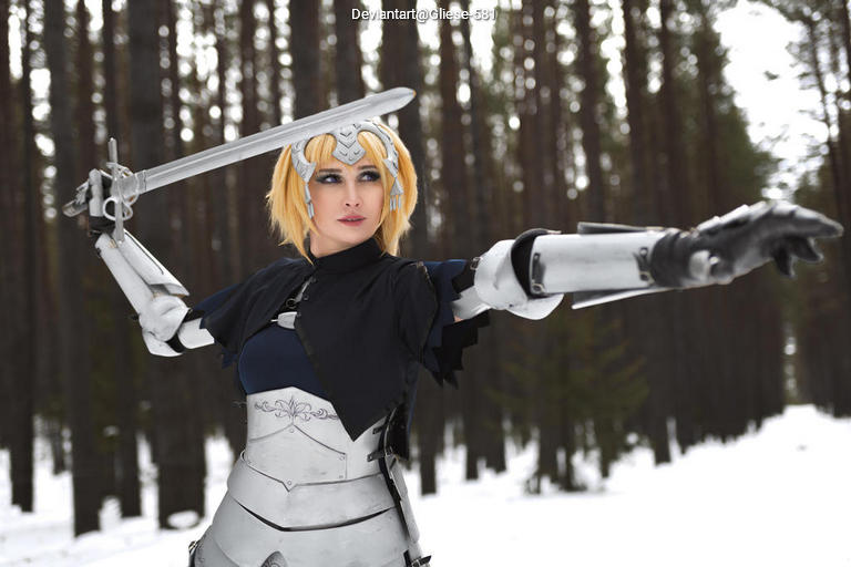 A person in a silver armor costume poses confidently in a snowy forest, holding a sword and pointing forward.