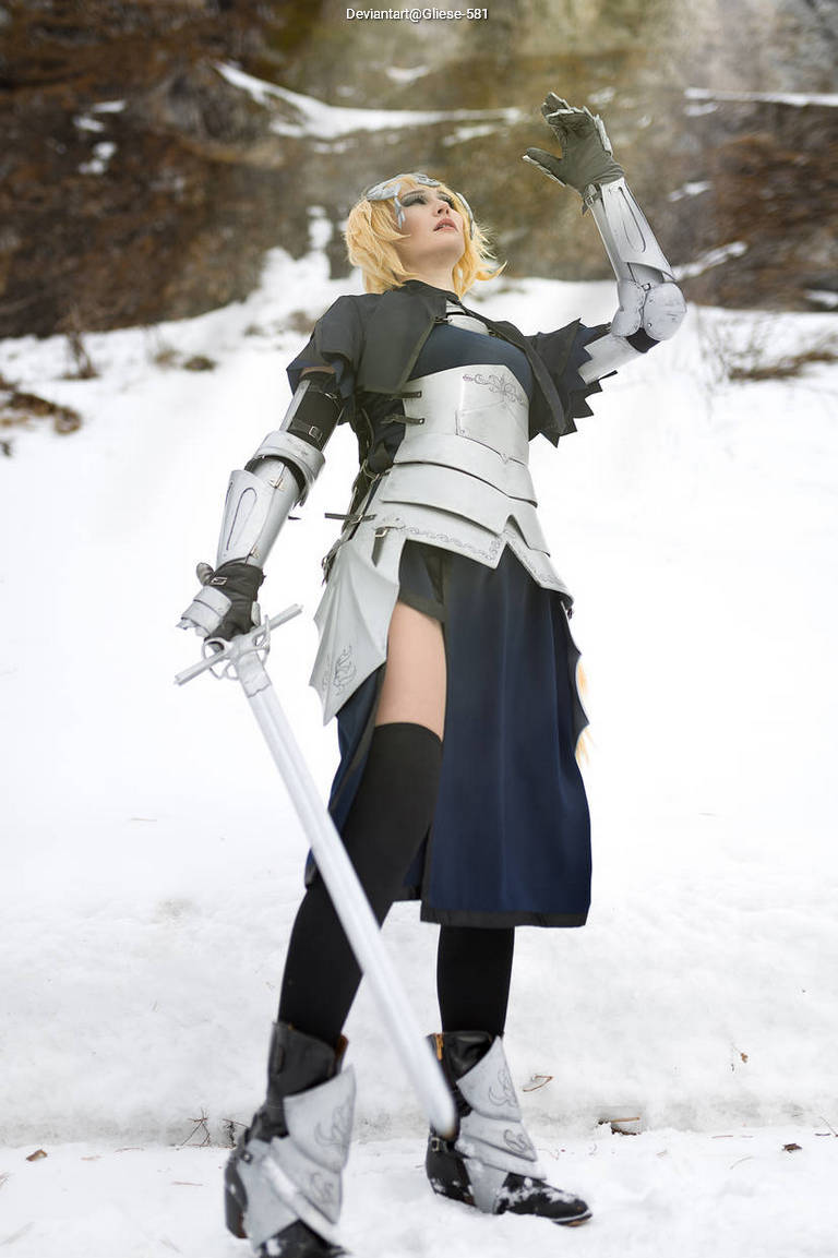 A person in a costume resembling a knight stands in a snowy landscape, holding a sword and looking up, with a determined expression. The outfit features metallic armor elements and a flowing skirt.