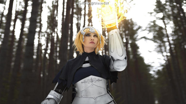 A person in a fantasy costume with silver armor and a cape, standing in a forest. They are holding a glowing, magical object in one hand, with a determined expression.