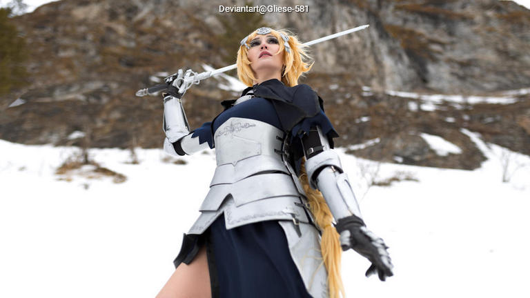 A person in a silver armor costume poses dramatically with a sword, set against a snowy backdrop and rocky hillside.