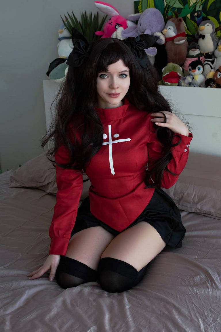 A person in a red outfit with a white cross sitting on a bed, surrounded by plush toys.